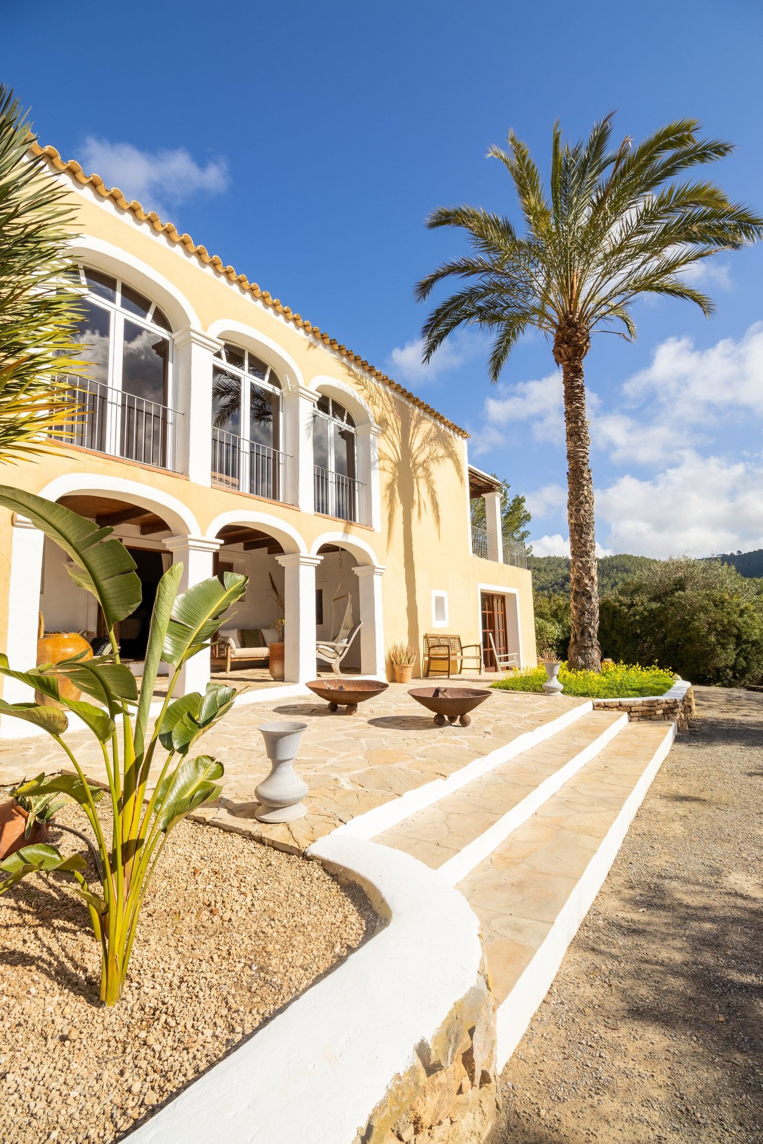 A yellow-washed Ibizan villa with arched terraces and a tall palm against a clear blue sky.