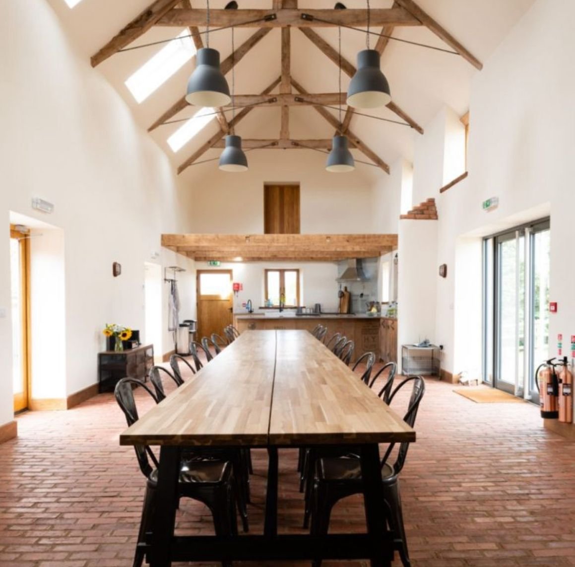A converted barn with exposed roof beams, a long shared table and brick floor set for a retreat.